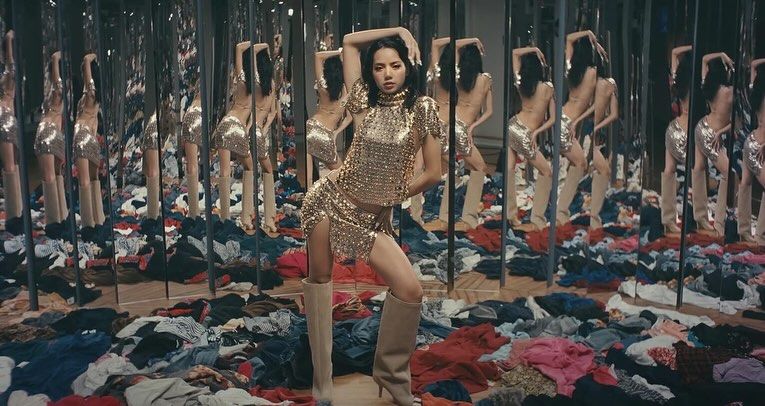 gaya kece lisa 'blackpink' dan  rosalía di music video 'new woman', 1. Lisa mengawali video musiknya dengan penampilan fierce. Memancarkan aura dark feminine, Ia pakai mantel hitam yang dikenakan di atas bra berkilauan dan celana pendek mikro yang serasi, dilengkapi dengan kalung hati metalik dan sepatu boots setinggi lutut., 2. Tampil dengan gaya a la gilded girl, Lisa pakai atasan metalik dan rok mini warna gold yang serasi. Suede boots warna nude dari Maison Margiela melengkapi gayanya., 3. Rosalía dengan gaya khasnya berikan sentuhan modern pada outfit yang terinspirasi dari flamenco. Ia mengenakan dress merah dengan potongan asimetris dengan garis leher rendah dipadukan dengan ankle boots merah. Warna merah yang berani menciptakan siluet dramatis yang kuat dan feminin., 4. Gaya Rosalía selanjutnya pakai bodysuit warna putih dengan motif floral merah dipadukan dengan heels hitam yang memancarkan nuansa vintage., 5. Dalam salah satu adegan, Lisa tampil fierce mengenakan pakaian bulu-bulu hitam, yang dipadukan dengan riasan mata gelap dan tatanan rambut sleek. , 6. Lisa bergaya edgy dengan atasan korset, celana kargo low-rise dan belt putih bergaya Y2K. Di adegan lainnya Ia melengkapi penampilannya dengan mantel bulu yang terinspirasi dari gaya Mob Wife yang vintage sekaligus berani., 7. Seperti Yin&amp;Yang, Lisa dan Rosalía mengenakan outfit hitam putih dengan dress berbahan sheer yang flowy., 8. Dalam adegan terakhir, Rosalía pakai mantel bertekstur warna pink yang dipadukan dengan kacamata biru reflektifnya yang memberi sentuhan modern. Di sampingnya, Lisa tampil kontras dengan outfit yang lebih edgy, mengenakan jaket kulit hitam dan putih dengan kacamata bergaya futuristik.