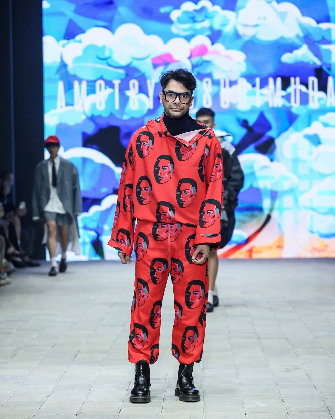 amotsyamsurimuda tampilkan koleksi 'sense of ease' di pimfw 2024, 1. AMOTSYAMSURIMUDA menampilkan koleksi terbarunya untuk Spring/Summer 2025 di perhelatan Plaza Indonesia Men’s Fashion Week. Bertajuk Sense of Ease, koleksi ini fokus pada penerimaan terhadap perjalanan hidup seseorang., 2. Mencerminkan beragam momen dan pengalaman yang dialami seseorang, Amot Syamsuri Muda memadukan elemen-elemen kontras pada pakaian seperti maskulin dan feminin, kemeja dan piyama, hingga pakaian formal dan informal., 3. Selain koleksi pakaian yang didominasi potongan loose, ada sentuhan menonjol pada sejumlah look dengan warna-warna yang pop-up dan motif bergambar wajah., 4. Perpaduan pakaian formal dan informal seperti kemeja dan piyama atau pakaian tidur memberikan sentuhan ‘ease’ di rangkaian koleksinya. Seperti perpaduan kemeja, dasi dan jaket denim yang dipadukan dengan celana pendek., 5. Sejumlah look menampilkan kemeja dengan potongan unik yang dibuat seperti cape atau jubah yang menjuntai ke belakang.