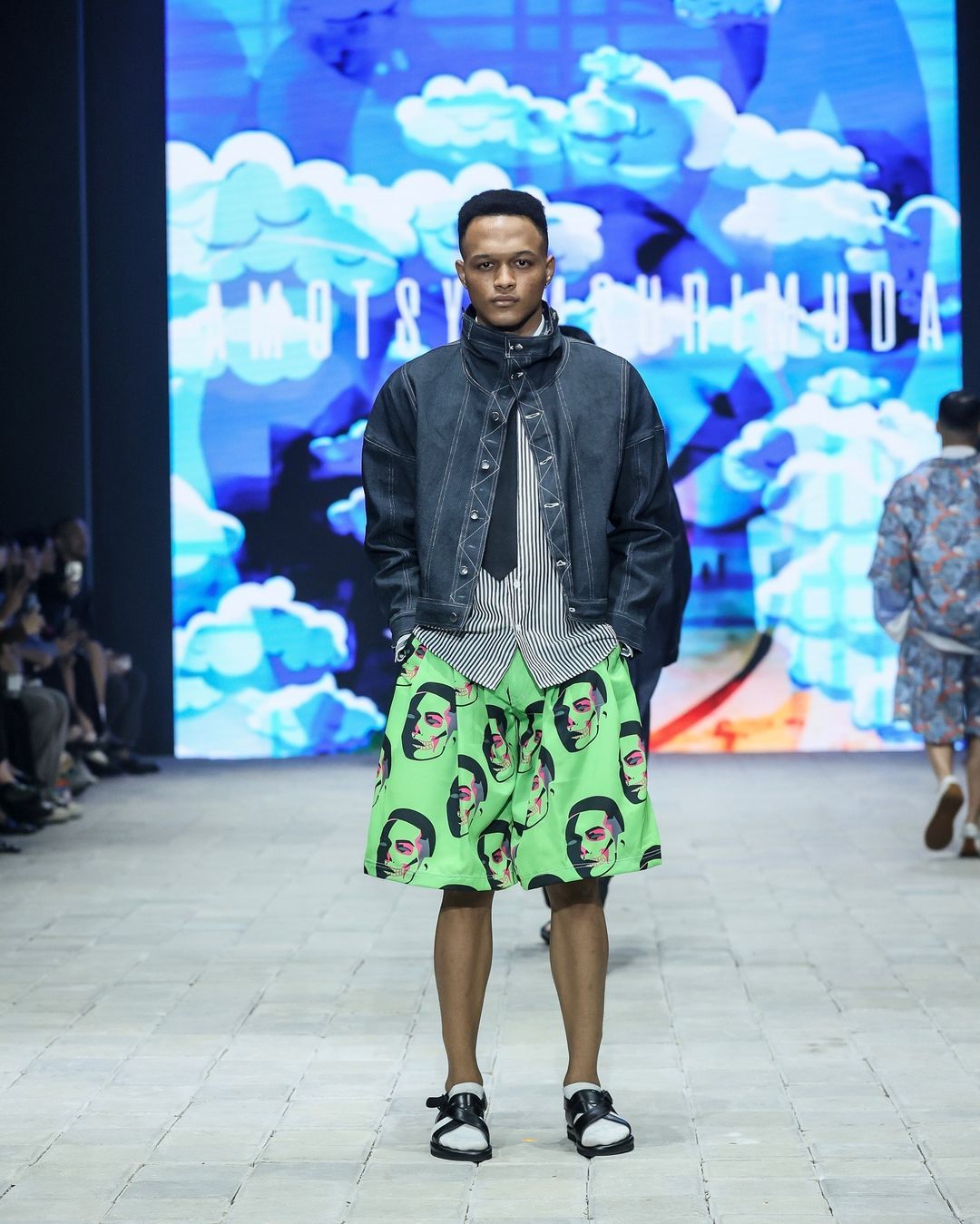 amotsyamsurimuda tampilkan koleksi 'sense of ease' di pimfw 2024, 1. AMOTSYAMSURIMUDA menampilkan koleksi terbarunya untuk Spring/Summer 2025 di perhelatan Plaza Indonesia Men’s Fashion Week. Bertajuk Sense of Ease, koleksi ini fokus pada penerimaan terhadap perjalanan hidup seseorang., 2. Mencerminkan beragam momen dan pengalaman yang dialami seseorang, Amot Syamsuri Muda memadukan elemen-elemen kontras pada pakaian seperti maskulin dan feminin, kemeja dan piyama, hingga pakaian formal dan informal., 3. Selain koleksi pakaian yang didominasi potongan loose, ada sentuhan menonjol pada sejumlah look dengan warna-warna yang pop-up dan motif bergambar wajah., 4. Perpaduan pakaian formal dan informal seperti kemeja dan piyama atau pakaian tidur memberikan sentuhan ‘ease’ di rangkaian koleksinya. Seperti perpaduan kemeja, dasi dan jaket denim yang dipadukan dengan celana pendek., 5. Sejumlah look menampilkan kemeja dengan potongan unik yang dibuat seperti cape atau jubah yang menjuntai ke belakang.