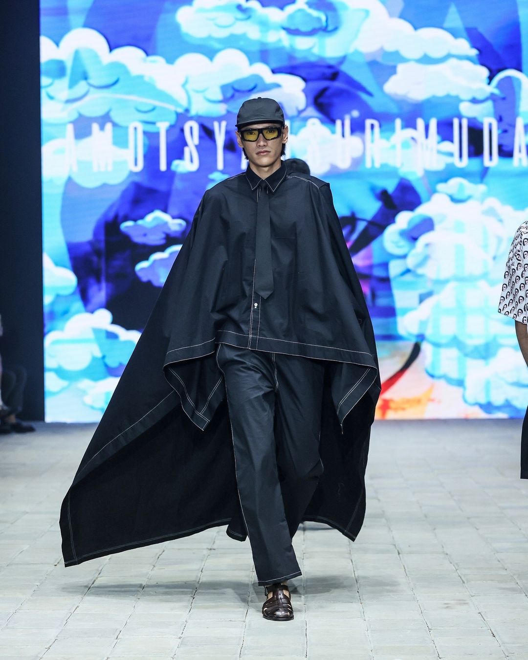 amotsyamsurimuda tampilkan koleksi 'sense of ease' di pimfw 2024, 1. AMOTSYAMSURIMUDA menampilkan koleksi terbarunya untuk Spring/Summer 2025 di perhelatan Plaza Indonesia Men’s Fashion Week. Bertajuk Sense of Ease, koleksi ini fokus pada penerimaan terhadap perjalanan hidup seseorang., 2. Mencerminkan beragam momen dan pengalaman yang dialami seseorang, Amot Syamsuri Muda memadukan elemen-elemen kontras pada pakaian seperti maskulin dan feminin, kemeja dan piyama, hingga pakaian formal dan informal., 3. Selain koleksi pakaian yang didominasi potongan loose, ada sentuhan menonjol pada sejumlah look dengan warna-warna yang pop-up dan motif bergambar wajah., 4. Perpaduan pakaian formal dan informal seperti kemeja dan piyama atau pakaian tidur memberikan sentuhan ‘ease’ di rangkaian koleksinya. Seperti perpaduan kemeja, dasi dan jaket denim yang dipadukan dengan celana pendek., 5. Sejumlah look menampilkan kemeja dengan potongan unik yang dibuat seperti cape atau jubah yang menjuntai ke belakang.