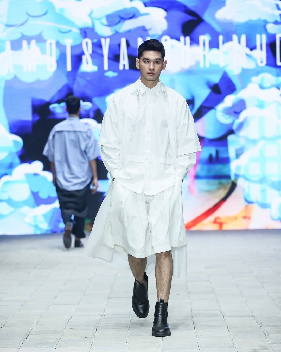 amotsyamsurimuda tampilkan koleksi 'sense of ease' di pimfw 2024, 1. AMOTSYAMSURIMUDA menampilkan koleksi terbarunya untuk Spring/Summer 2025 di perhelatan Plaza Indonesia Men’s Fashion Week. Bertajuk Sense of Ease, koleksi ini fokus pada penerimaan terhadap perjalanan hidup seseorang., 2. Mencerminkan beragam momen dan pengalaman yang dialami seseorang, Amot Syamsuri Muda memadukan elemen-elemen kontras pada pakaian seperti maskulin dan feminin, kemeja dan piyama, hingga pakaian formal dan informal., 3. Selain koleksi pakaian yang didominasi potongan loose, ada sentuhan menonjol pada sejumlah look dengan warna-warna yang pop-up dan motif bergambar wajah., 4. Perpaduan pakaian formal dan informal seperti kemeja dan piyama atau pakaian tidur memberikan sentuhan ‘ease’ di rangkaian koleksinya. Seperti perpaduan kemeja, dasi dan jaket denim yang dipadukan dengan celana pendek., 5. Sejumlah look menampilkan kemeja dengan potongan unik yang dibuat seperti cape atau jubah yang menjuntai ke belakang.
